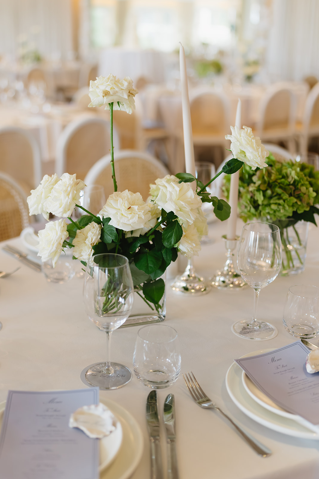 Reception table styled with white roses in glass vases, tall candles and green hydrangeas