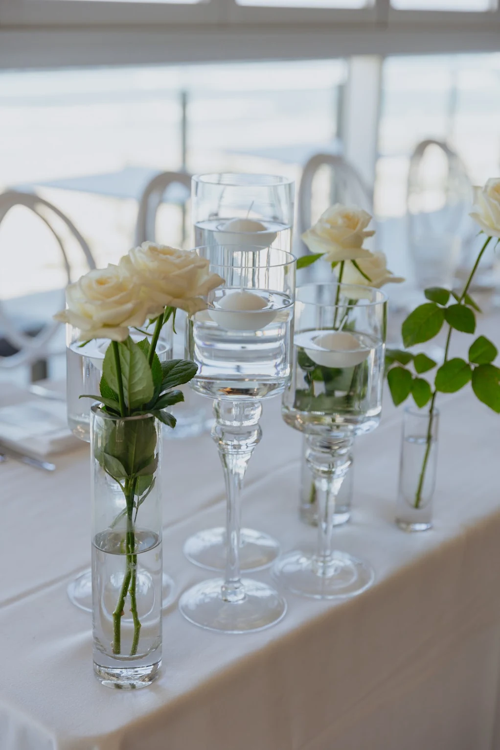 White roses and floating candles styled in glass vases on an event table