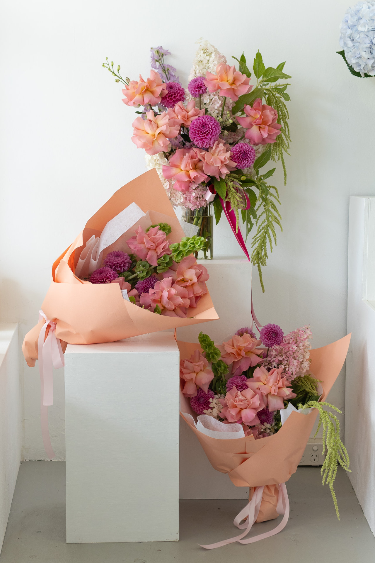 Peach and pink bouquets wrapped and ready on white plinths