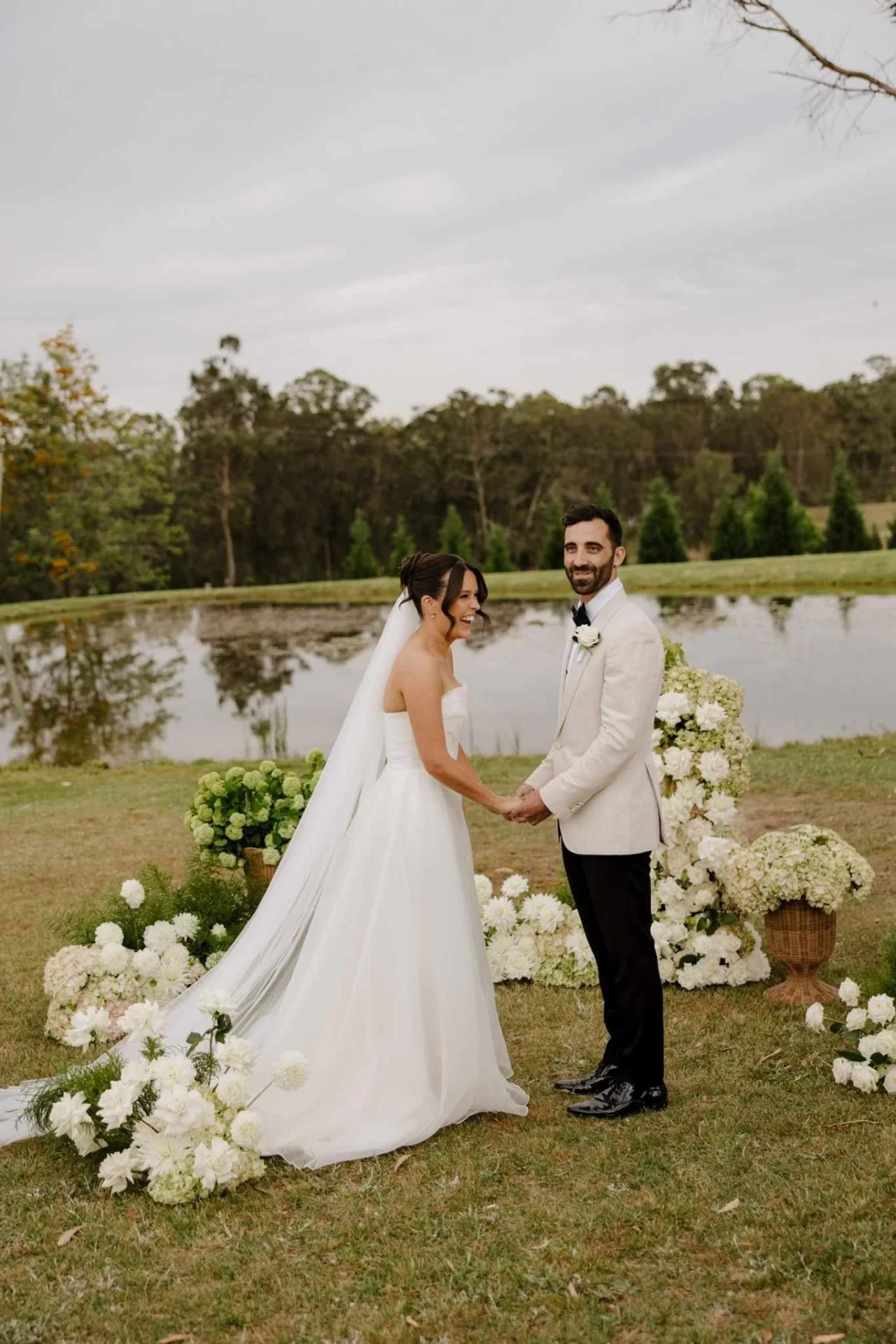 Newlyweds beside the lake framed by white and green wedding florals