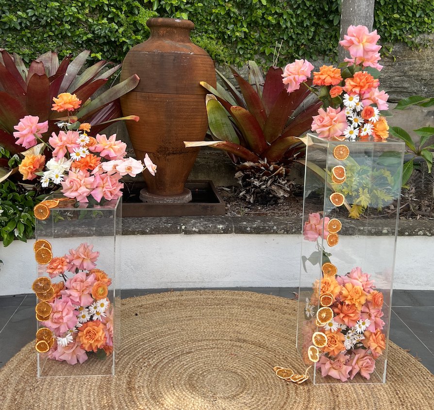 Acrylic plinths filled with pink and orange flowers and dried citrus for DIY hire