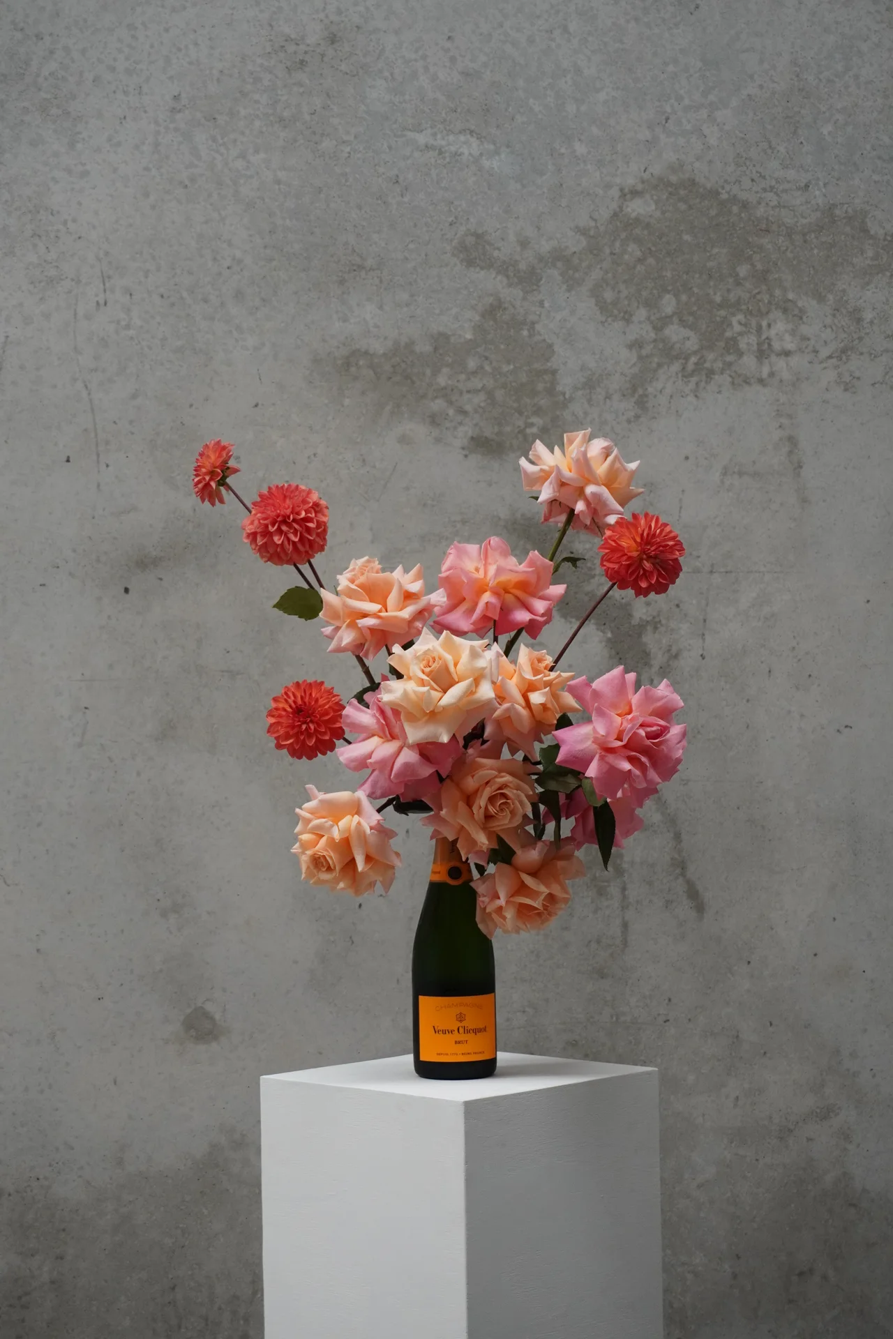 Roses and dahlias arranged in a champagne bottle on a plinth