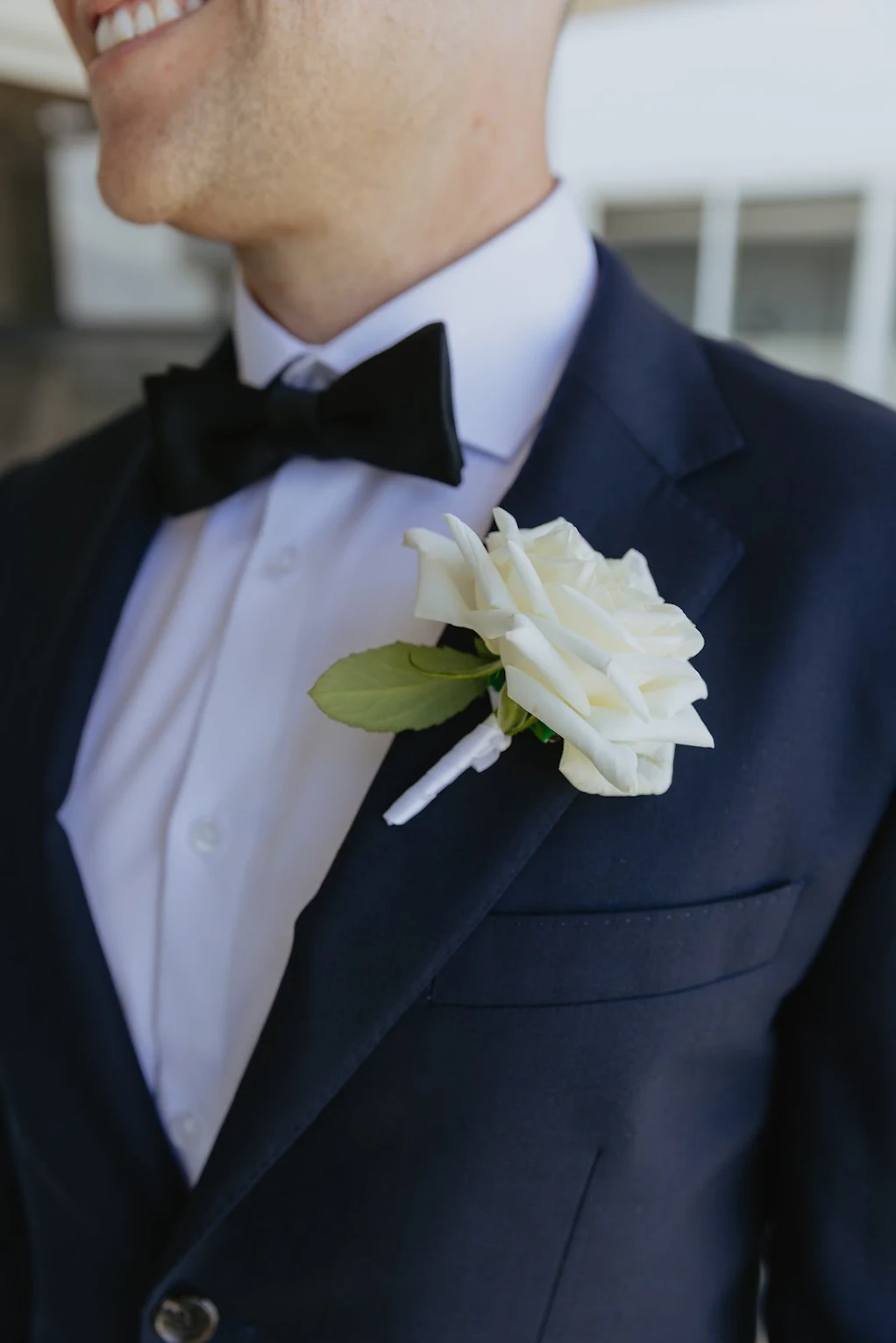 White rose buttonhole pinned to a navy suit with a black bow tie