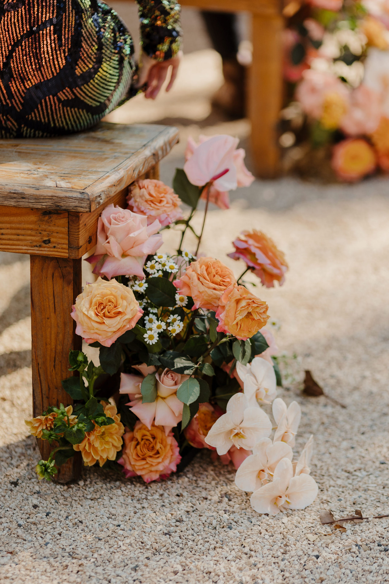 Orchids and apricot roses spilling from a timber bench onto the gravel