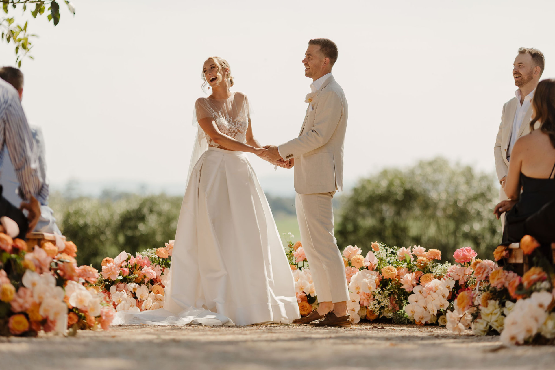 Bride and groom laughing at the ceremony, framed by peach and ivory floral meadows