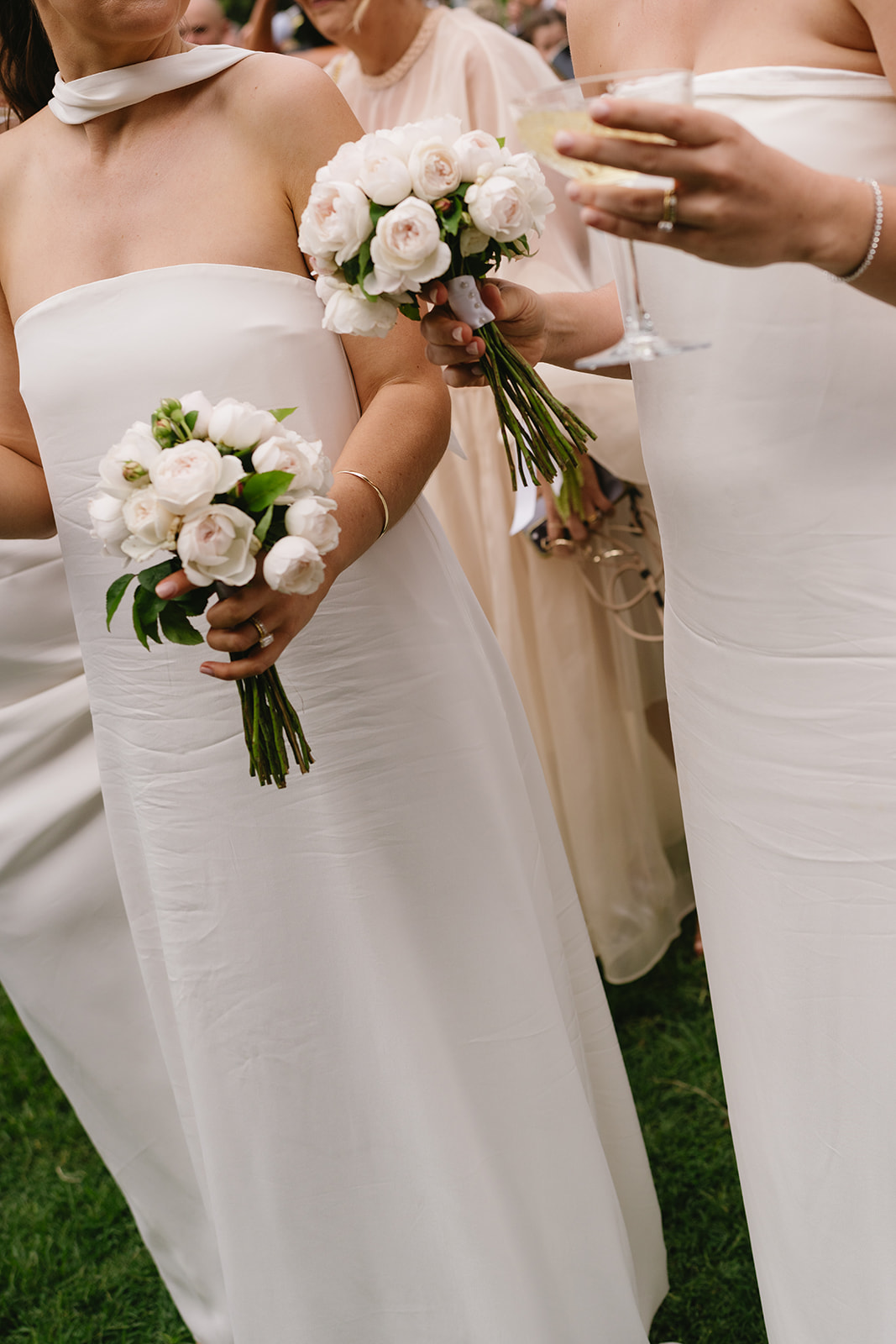 Bridesmaids in white dresses holding small bouquets of white and blush roses