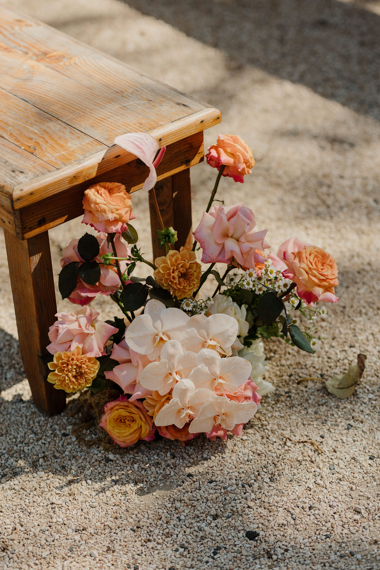 Peach roses, dahlias, orchids and daisies arranged along a weathered timber bench