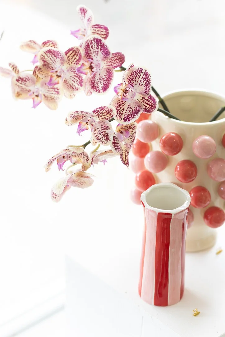 Speckled orchids arranged in sculptural pink and red ceramic vessels